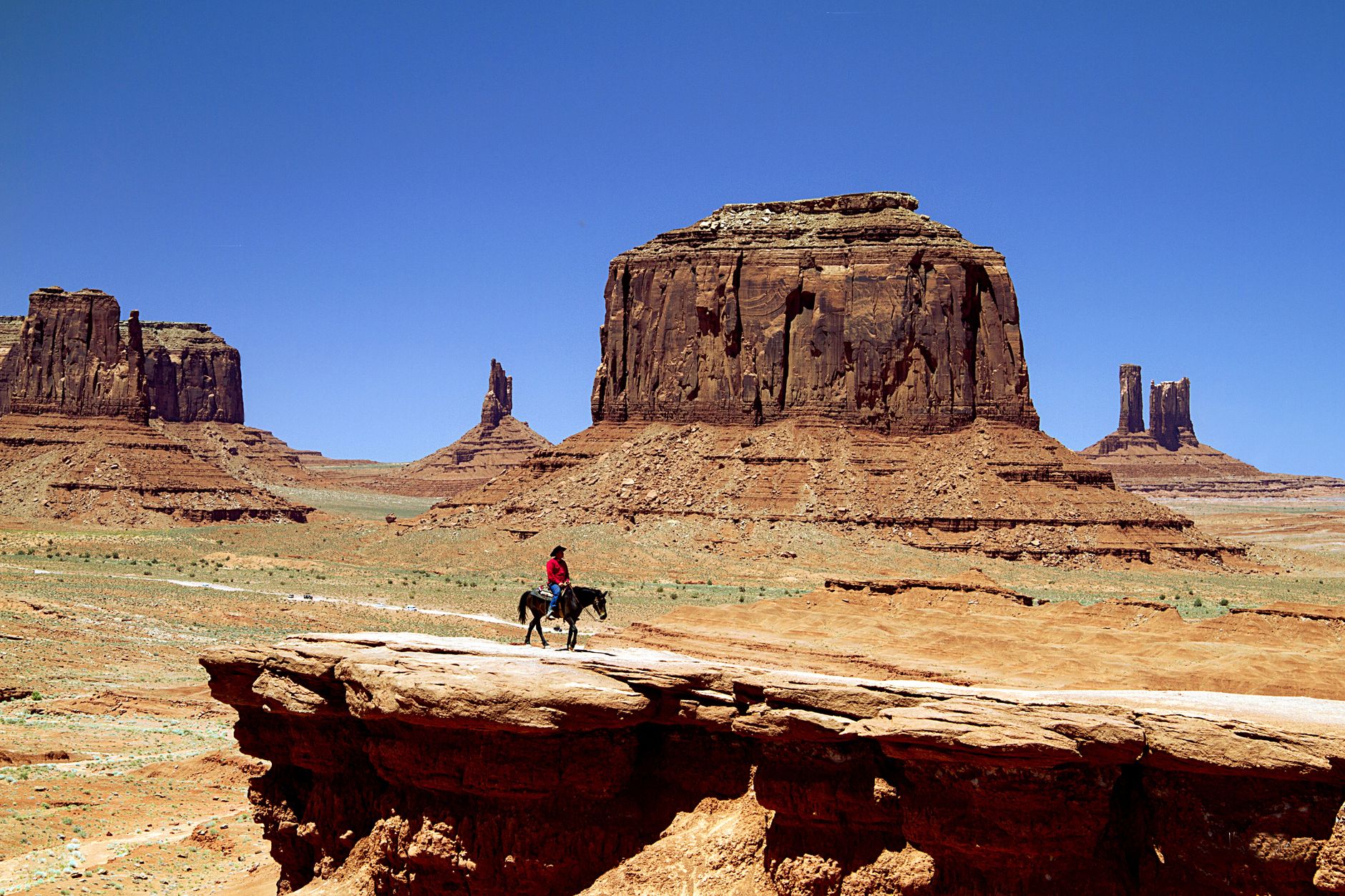 Horse rider traverses the stunning Monument Valley mesas under a clear blue sky.